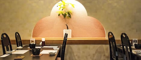 Un comedor con una mesa larga, sillas negras, una planta en maceta y una pared decorativa con un diseño de olas.