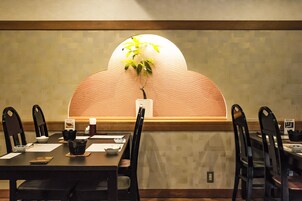 Un comedor con una mesa larga, sillas negras, una planta en maceta y una pared decorativa con un diseño de olas.