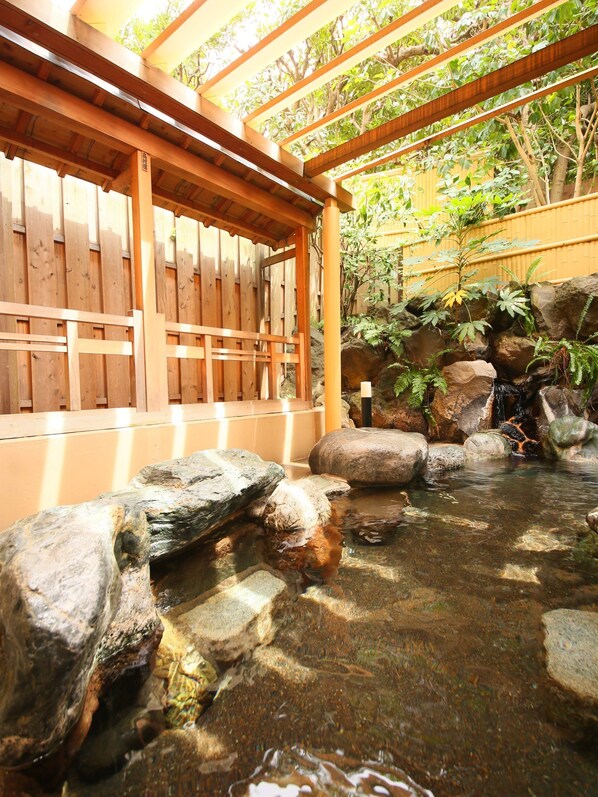 Una estructura de pérgola de madera con vista despejada a una pequeña fuente rodeada de rocas y plantas.