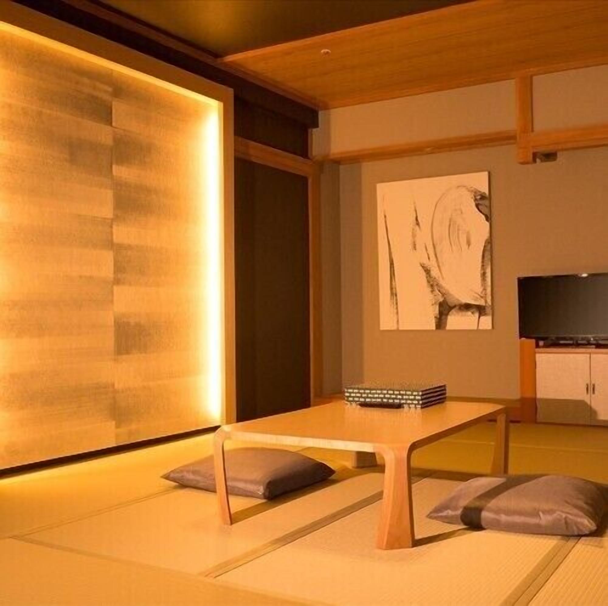A room with tatami flooring, a low wooden table, cushions, a television, and a painting on the wall.