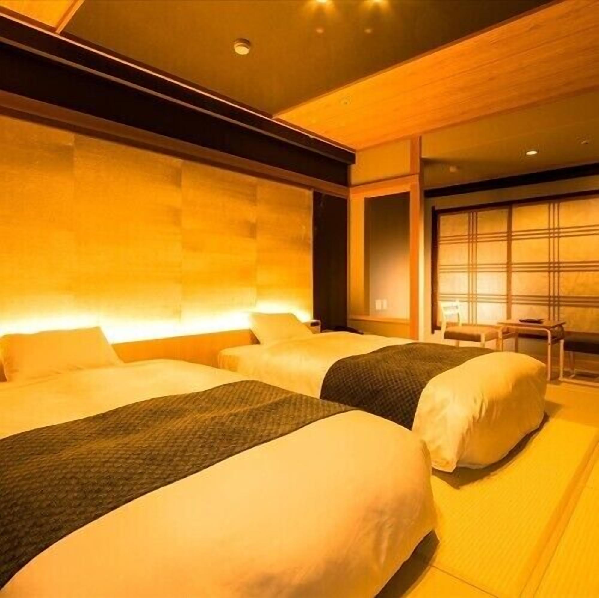 A hotel room with two beds, a wooden headboard, a small table, and a window with blinds.