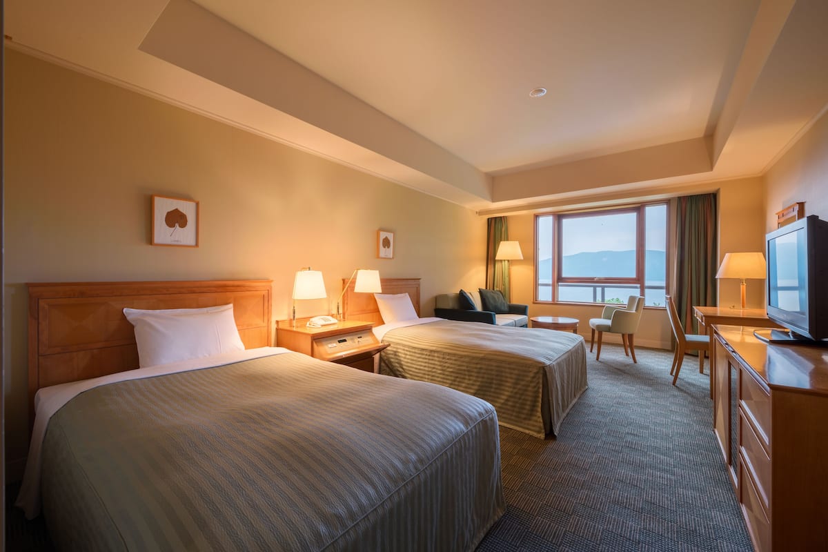 A hotel room with two beds, a desk, a television, and a window with a view.