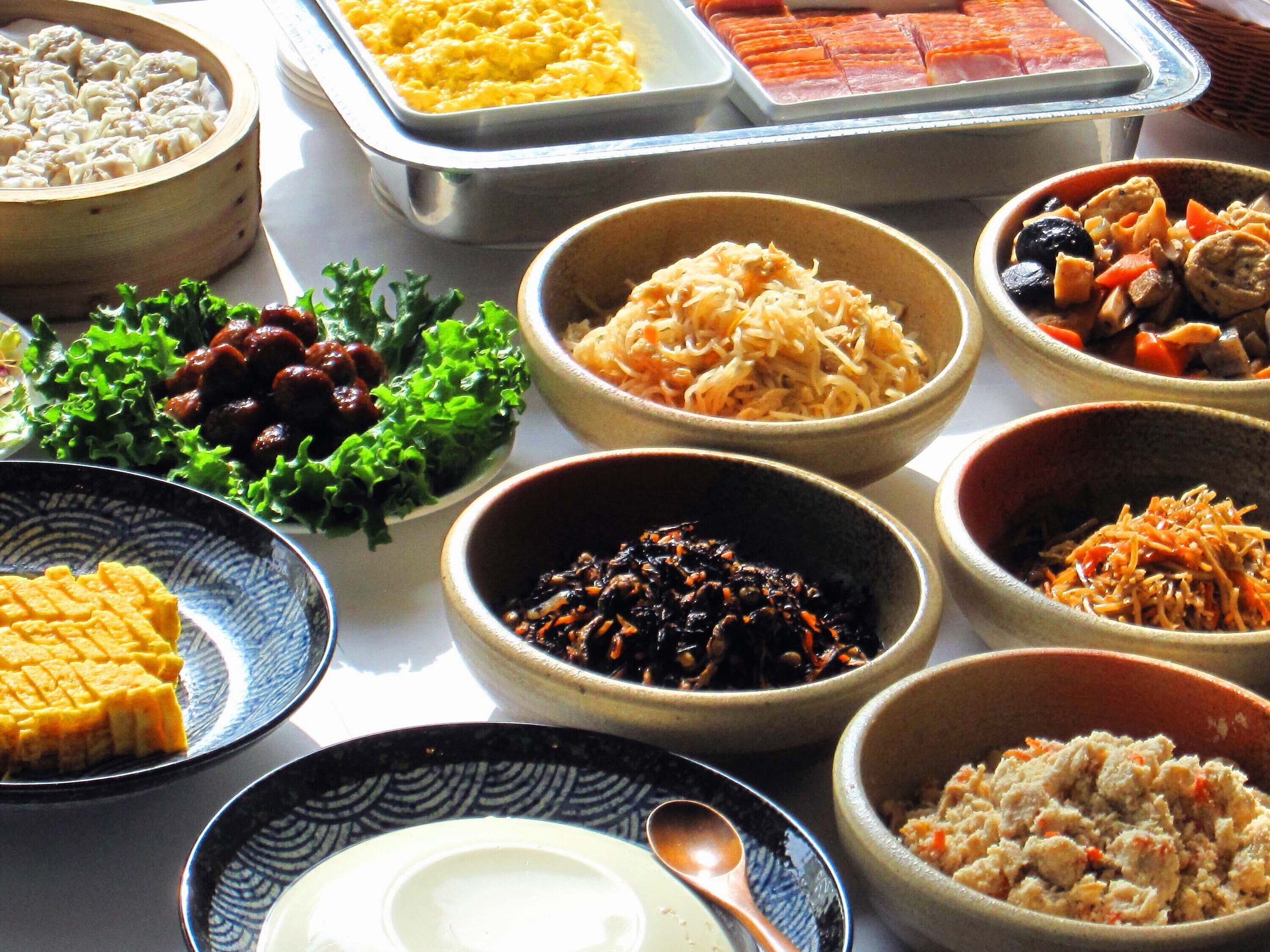 A variety of dishes arranged on a table, including dumplings, scrambled eggs, and different types of salads and side dishes.