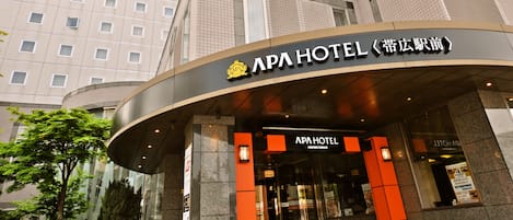 The exterior of APA Hotel with a modern design, featuring a curved entrance and a prominent sign.