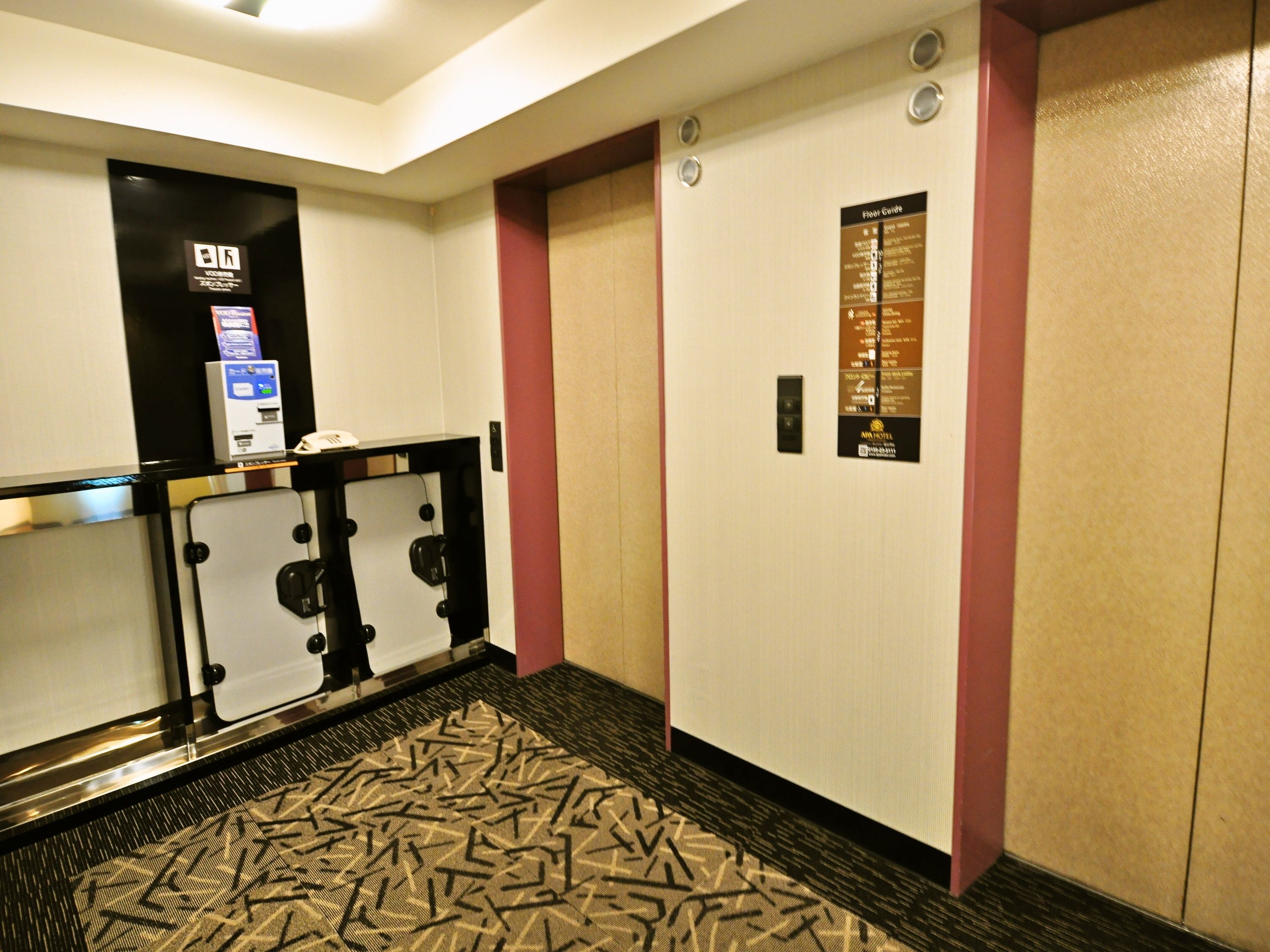 A hotel lobby with a reception desk, a floor map, and a wall-mounted elevator control panel.