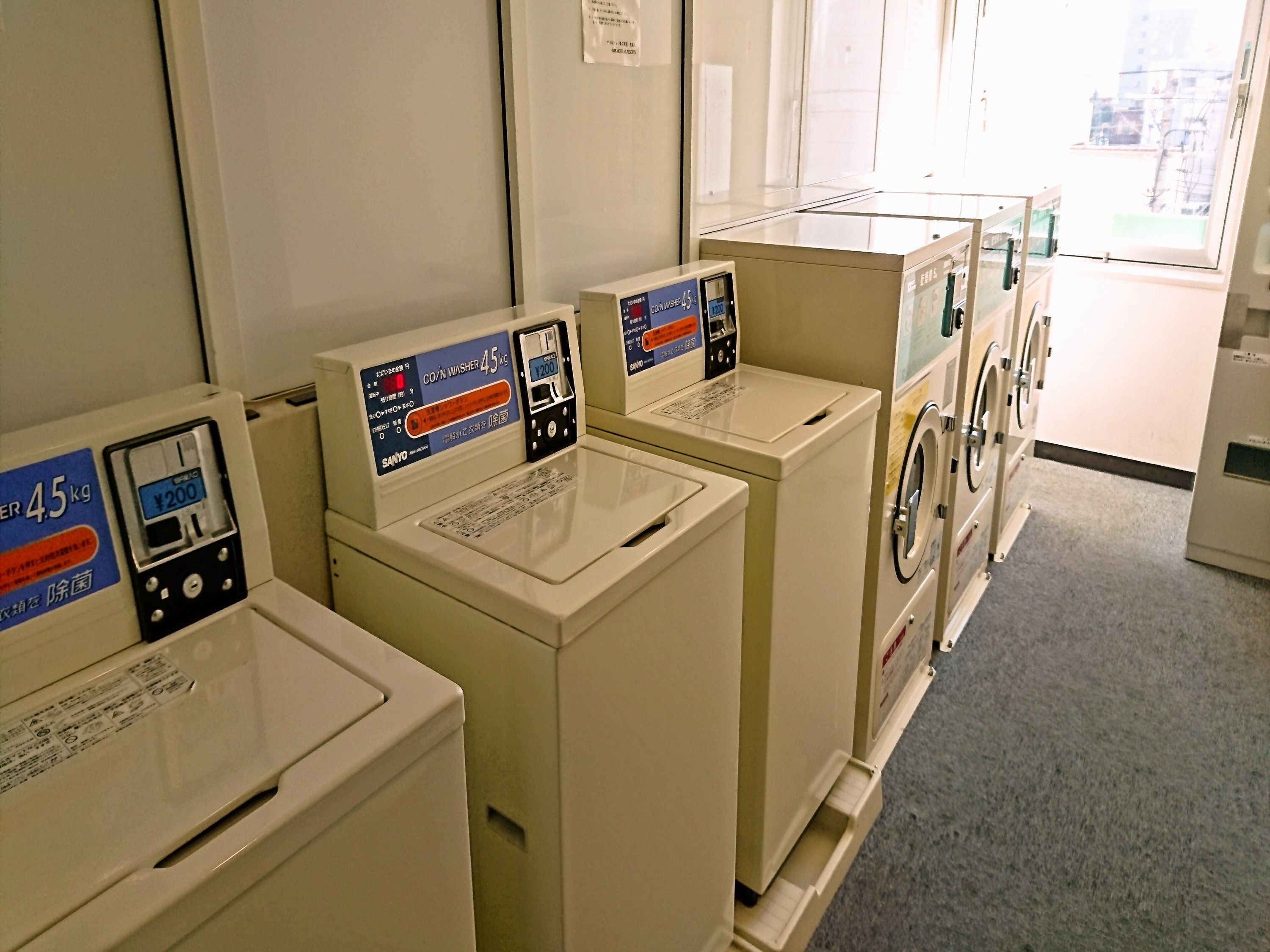 A row of coin-operated washing machines in a public area, each with a digital display and a price tag.