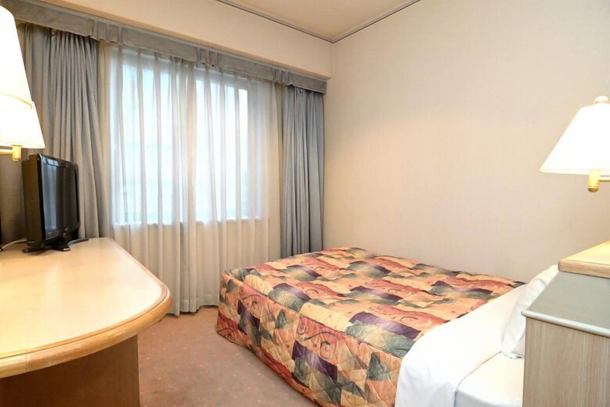 A hotel room with a bed, a desk, a chair, a television, and a window with curtains.