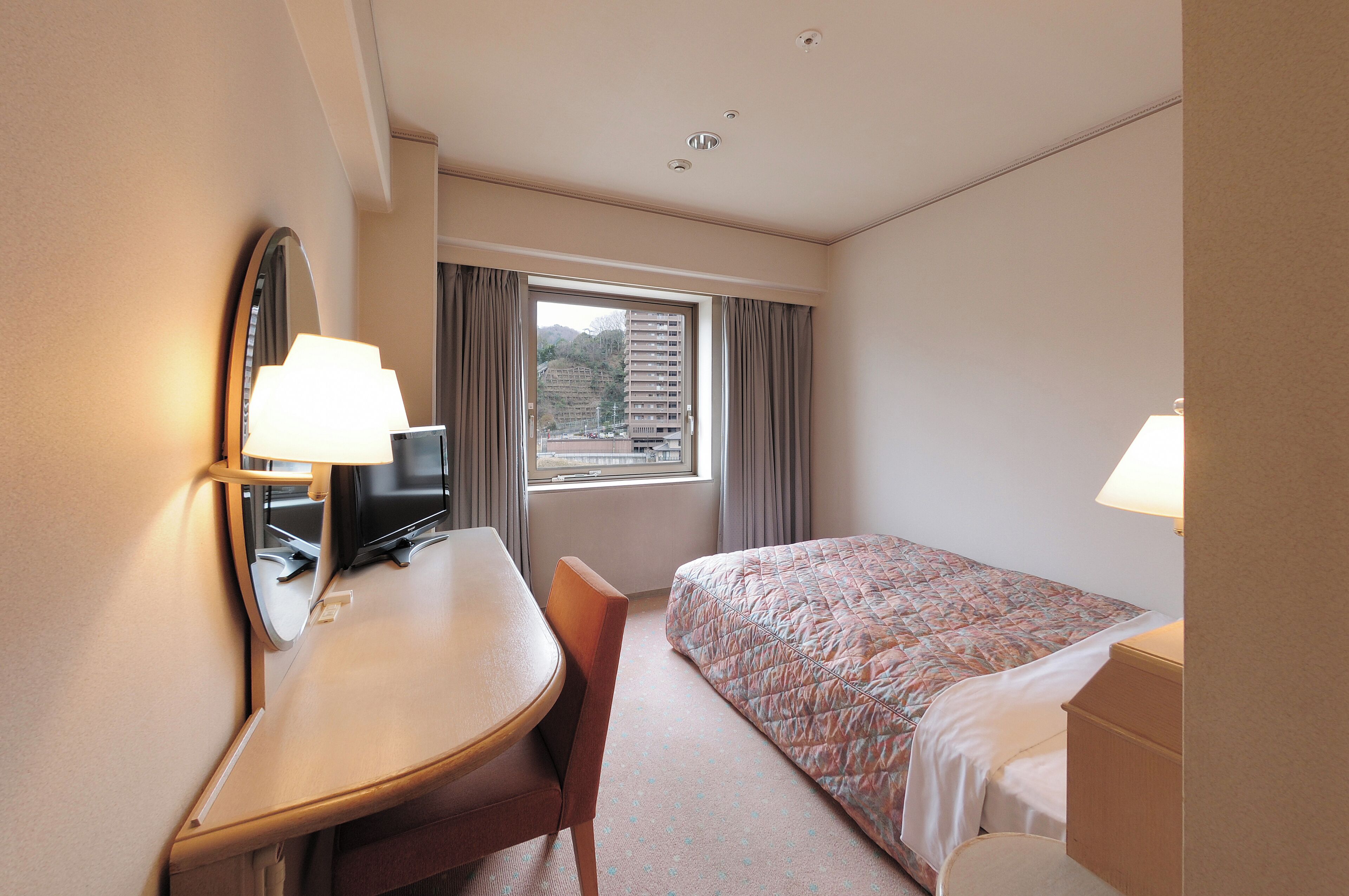 Una habitación de hotel con cama, escritorio, silla y ventana con cortinas.