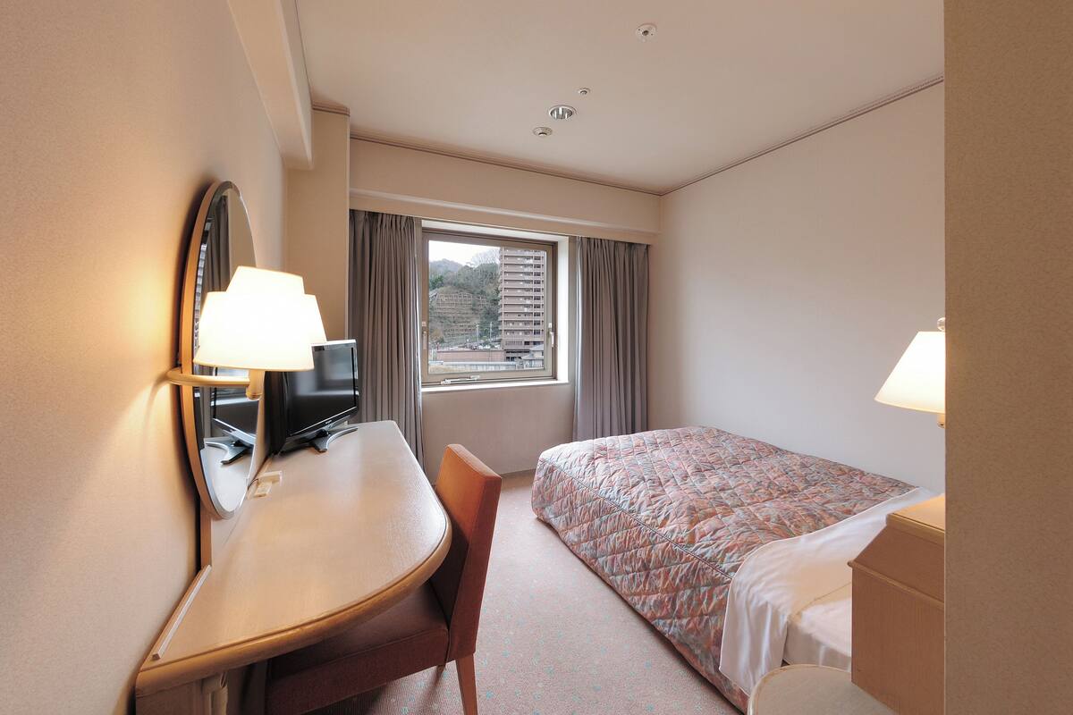 A hotel room with a bed, desk, chair, and a window with curtains.
