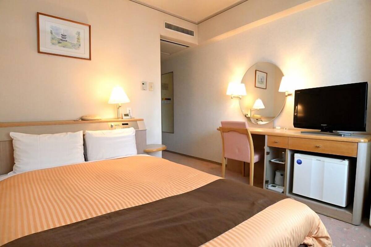 A hotel room with a bed, desk, chair, television, and a small refrigerator.