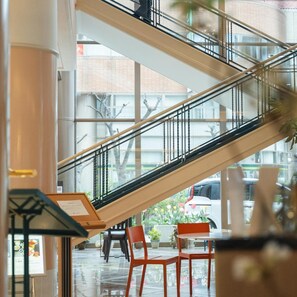 Un espacio interior con una escalera de cristal, una mesa con sillas y vistas al exterior.