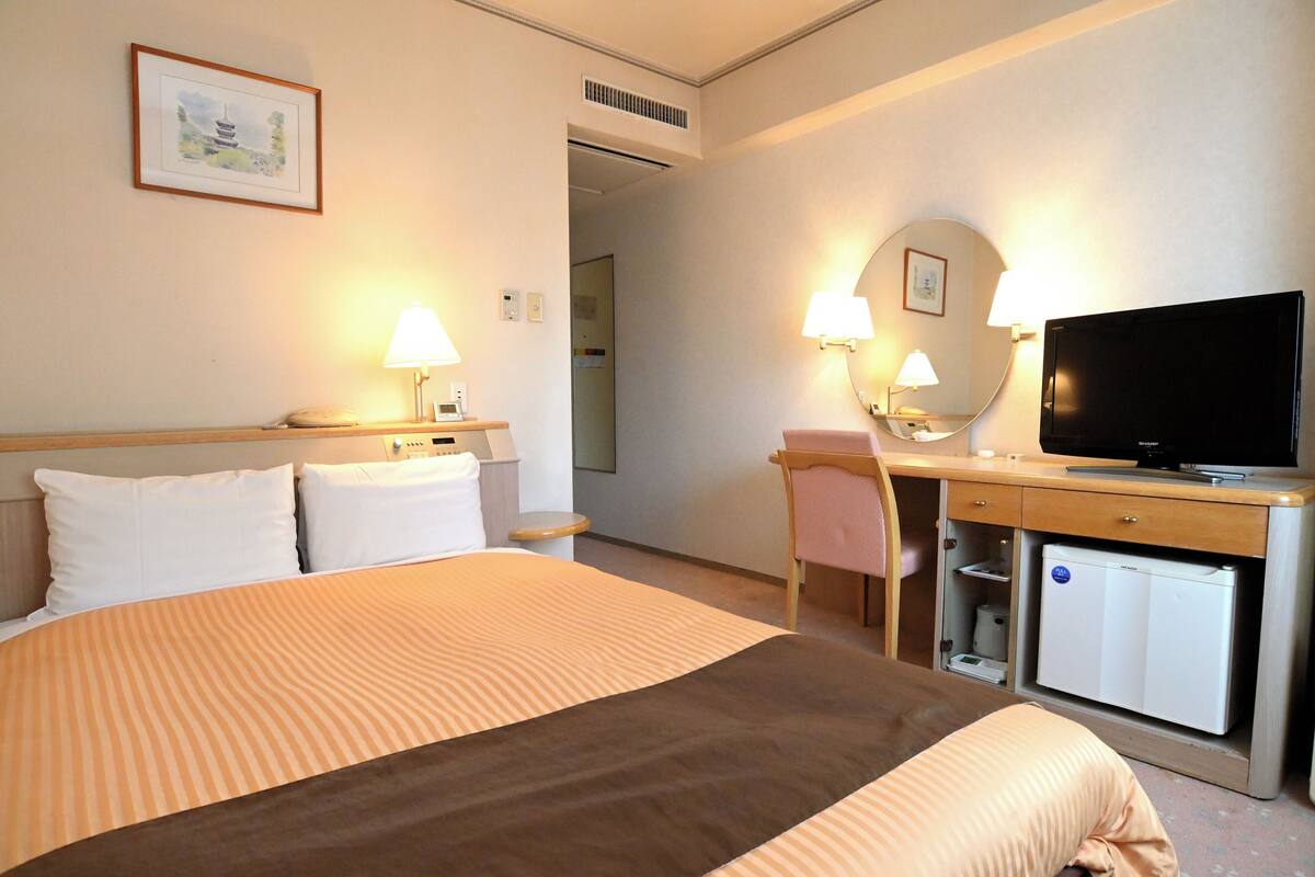 A hotel room with a bed, desk, television, and a small refrigerator.