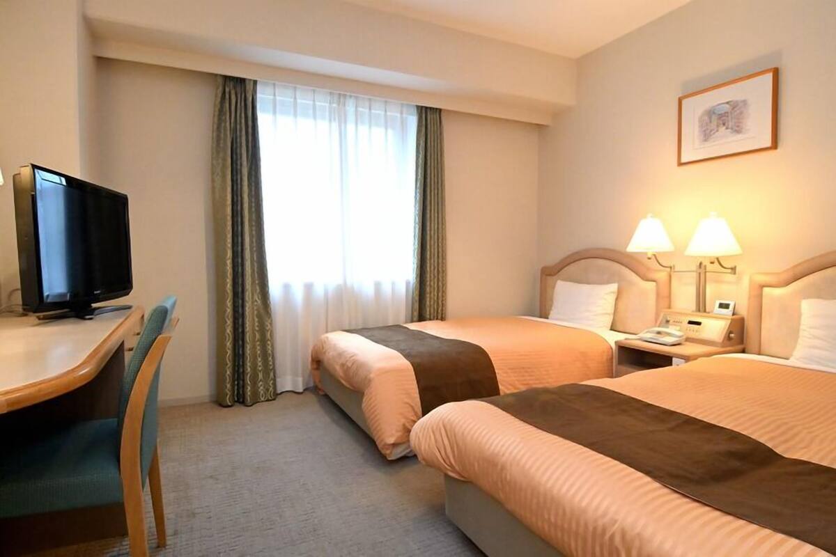 A hotel room with two beds, a desk with a television, and a window with curtains.