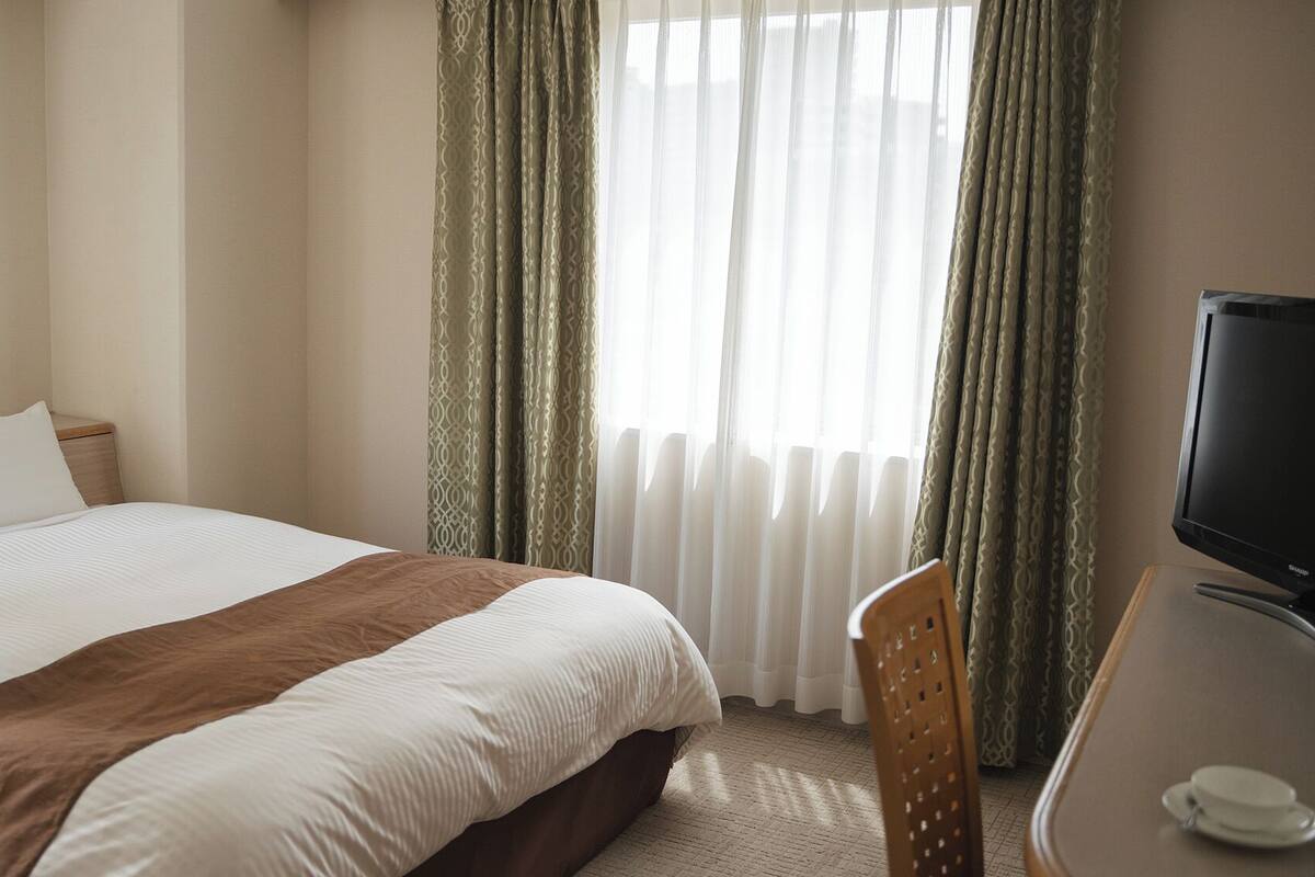 A hotel room with a bed, a desk with a television, and a framed picture on the wall.