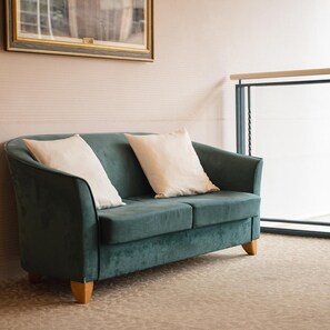 A teal sofa with wooden legs and two white cushions in a room with a patterned carpet.