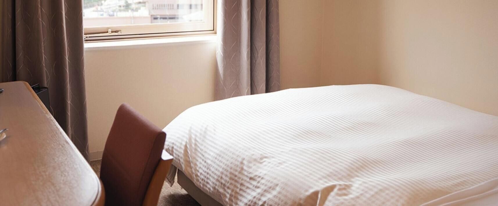 Hotellihuone, jossa on sänky, tuoli, työpöytä ja ikkuna, jossa on verhot.