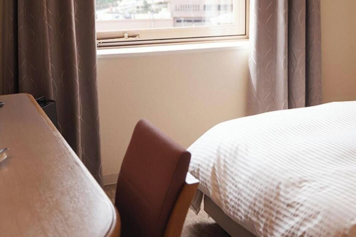 A hotel room with a bed, a chair, a desk, and a window with curtains.