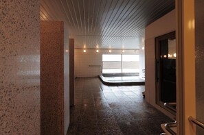 A corridor with a wet floor, a metal railing, and a glass door leading to a bright room with a view. - Takarazuka Washington Hotel (Takarazuka)