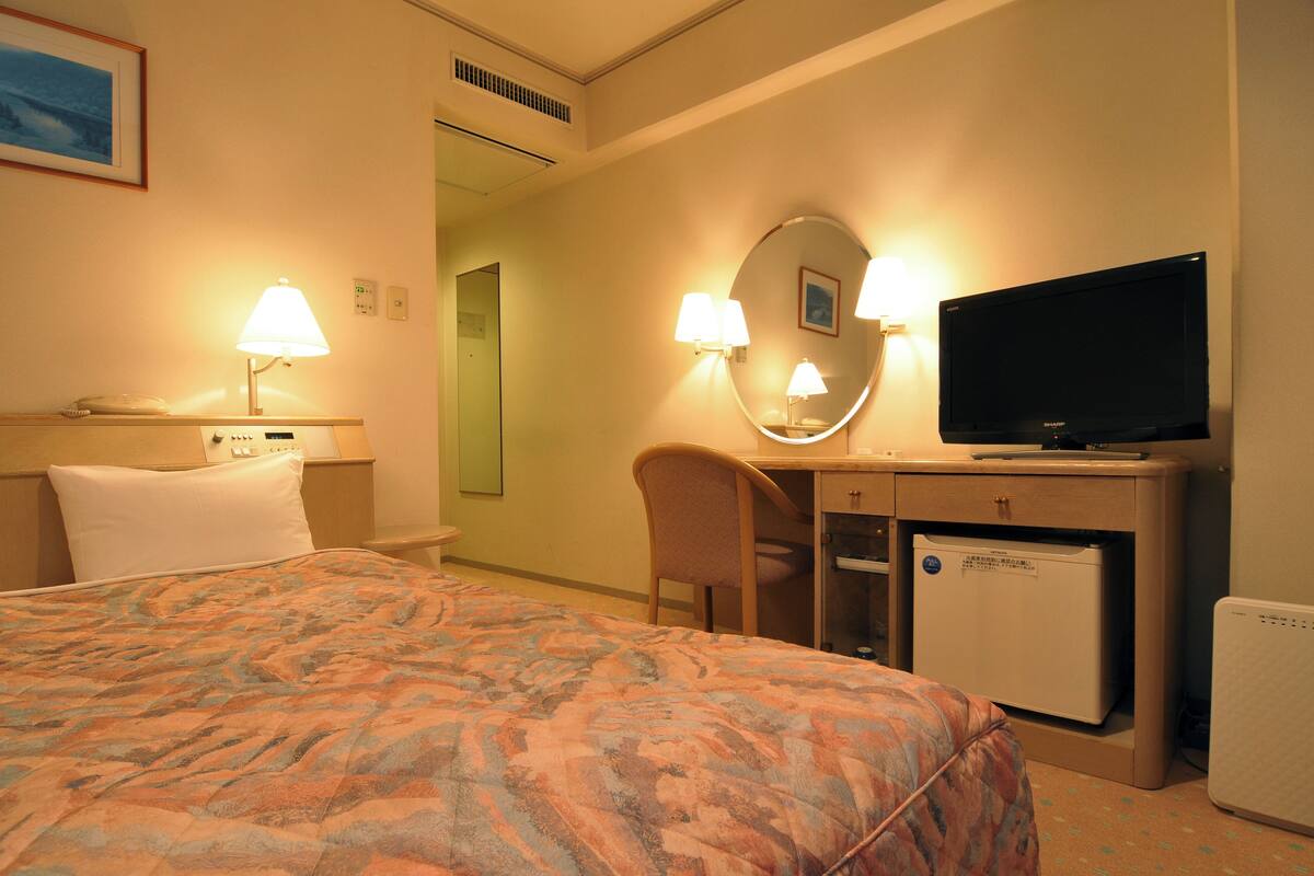 A hotel room with a bed, desk, television, and a mini-fridge.