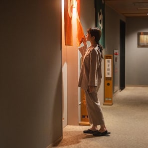 Una persona in un corridoio con pavimento tappezzato, un ascensore a parete e una porta con un cartello in lingua straniera.