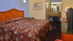 A hotel room with a large bed, a desk with a television, a chair, a bathroom mirror, and a framed picture on the wall. - Rodeway Inn (Sacramento)
