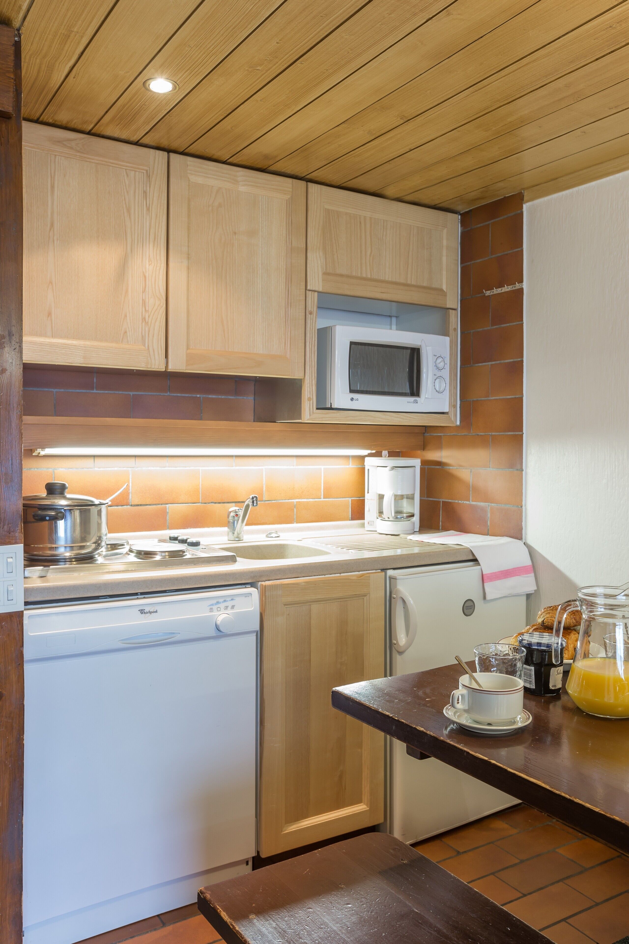 A compact kitchen with wooden cabinets, a microwave, a coffee maker, and a dishwasher.