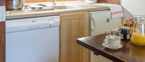 A compact kitchen with wooden cabinets, a microwave, a coffee maker, and a dishwasher.