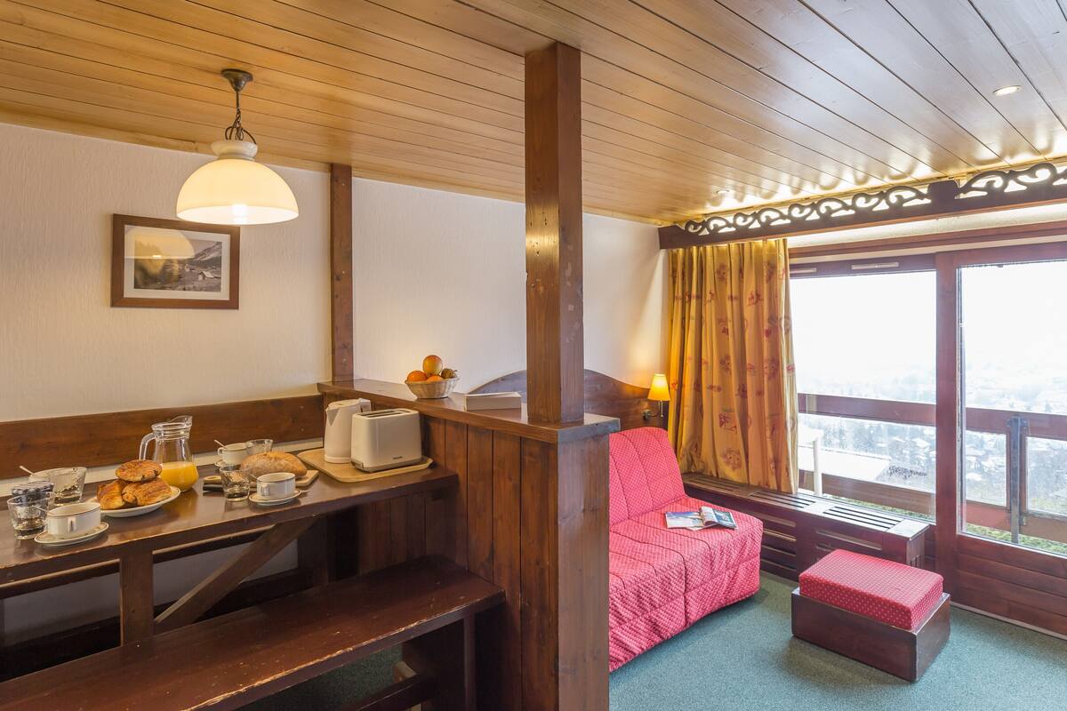 Ein gemütliches Zimmer mit Holzboden, einem Esstisch, der mit dem Frühstück gedeckt ist, einer roten gepolsterten Bank und einem Fenster mit Aussicht.
