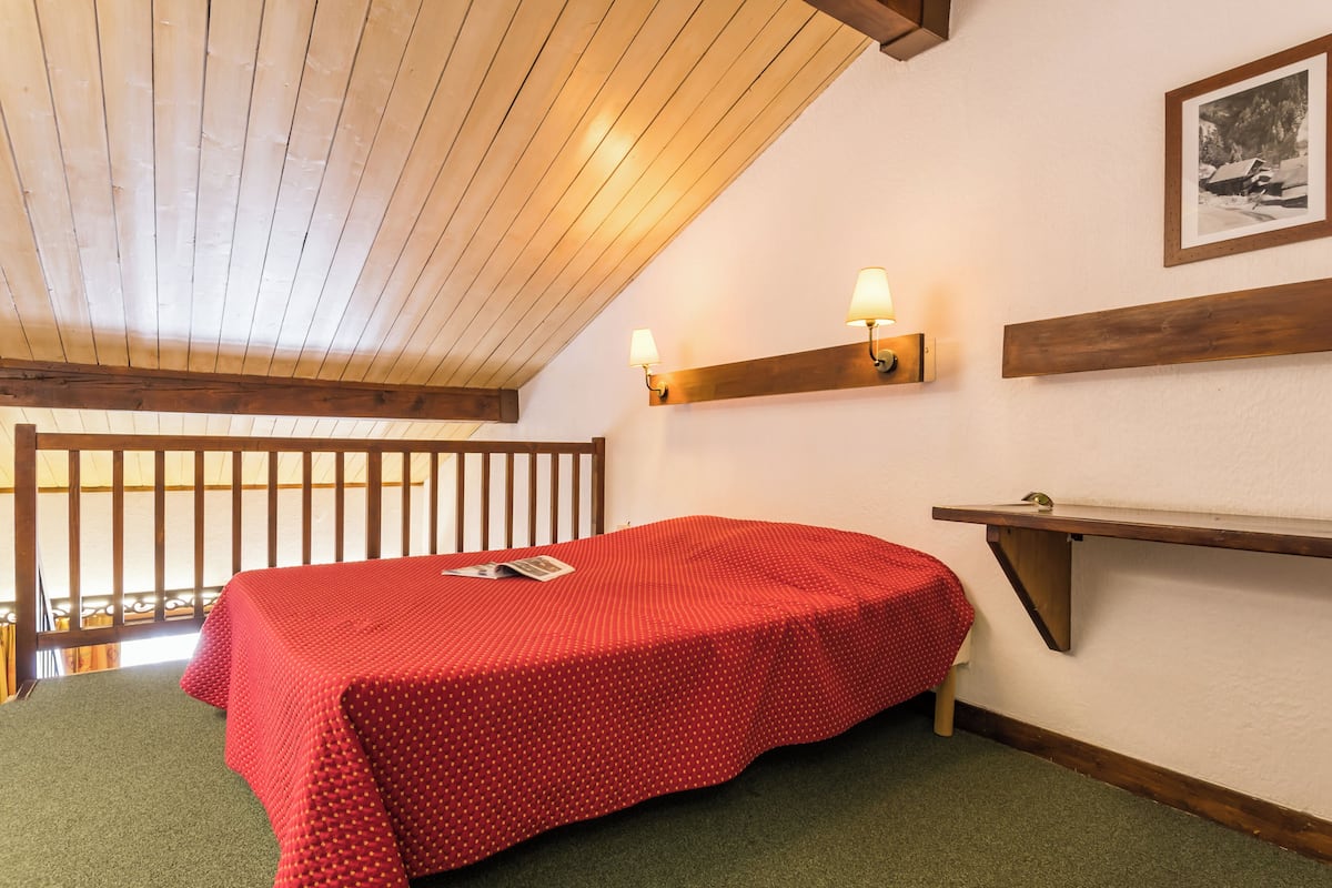 Ein Zimmer mit einem Bett, Holzbalken, einer an der Wand befestigten Ablagefläche und einem gerahmten Bild.