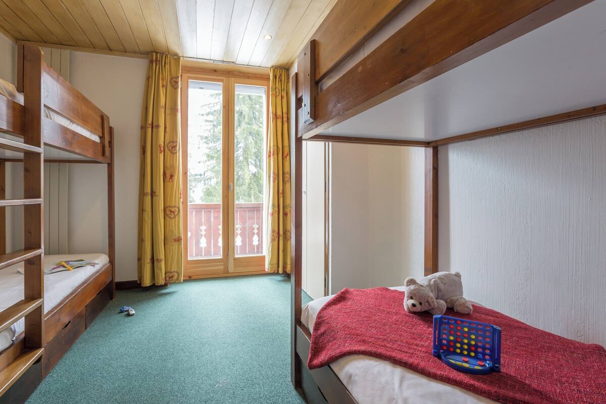 Ein Zimmer mit Etagenbetten, einem kleinen Tisch und einem Fenster mit Vorhängen.