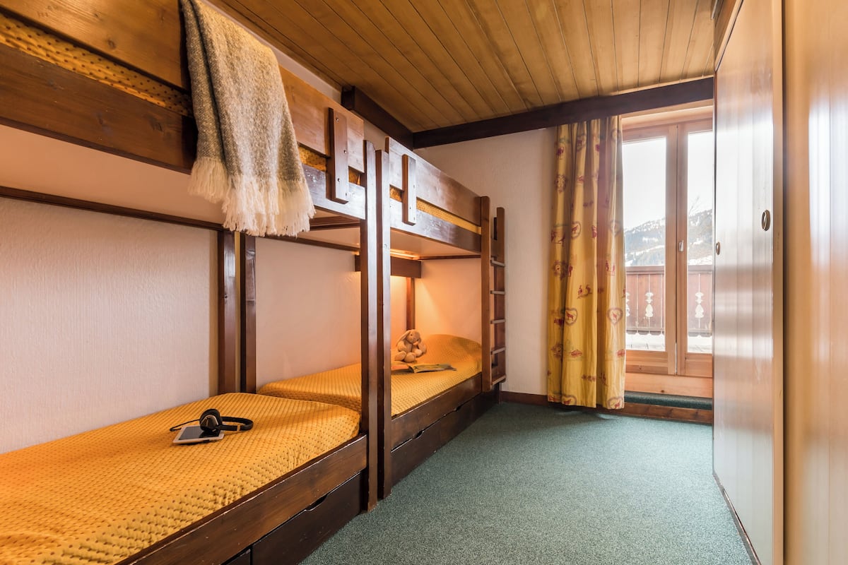 Ein Schlafsaalzimmer mit Etagenbetten, einem kleinen Schreibtisch und einem Fenster mit Vorhängen.