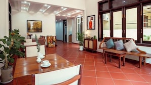 A spacious lobby with a wooden reception desk, a sofa with cushions, potted plants, and artwork on the walls. - An Hien Homestay Hoi An (Da Nang)