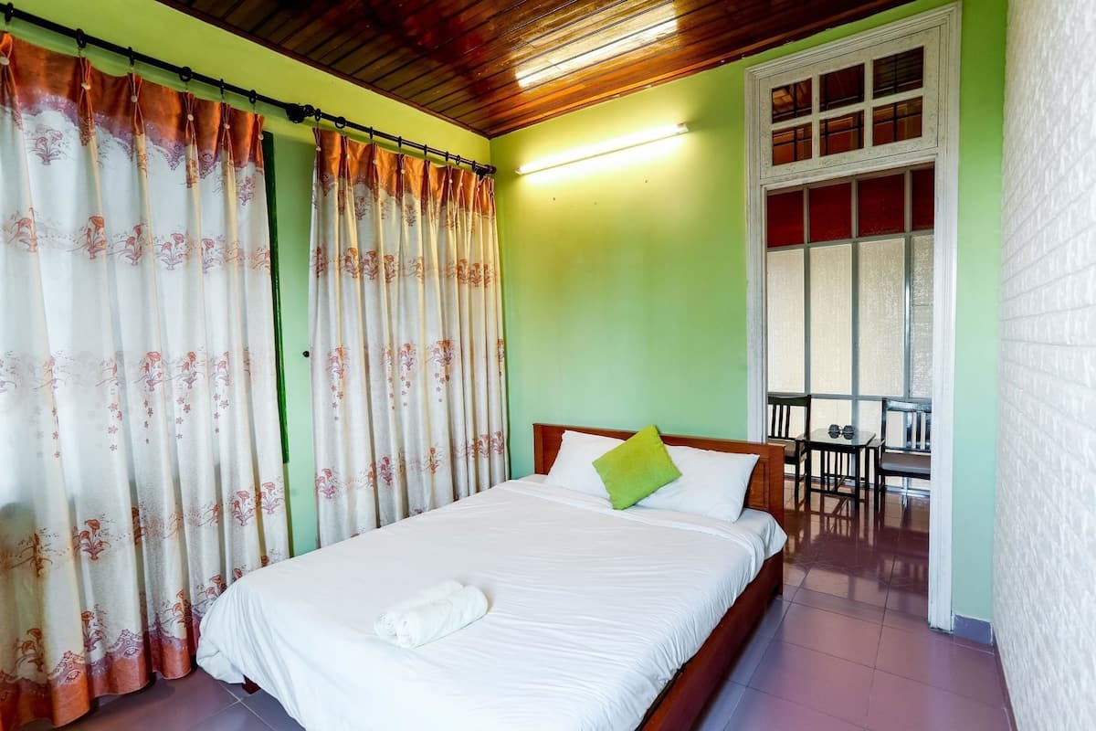 A room with a bed, a bench, a table, and a window with curtains.
