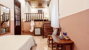 A hotel room with a bed, a wooden table with a vase and bottles, a small fridge, and a staircase with a railing. - An Hien Homestay Hoi An (Da Nang)