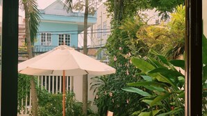 An outdoor seating area with a table and chairs under a large umbrella, surrounded by lush greenery and a building in the background. - An Hien Homestay Hoi An (Da Nang)