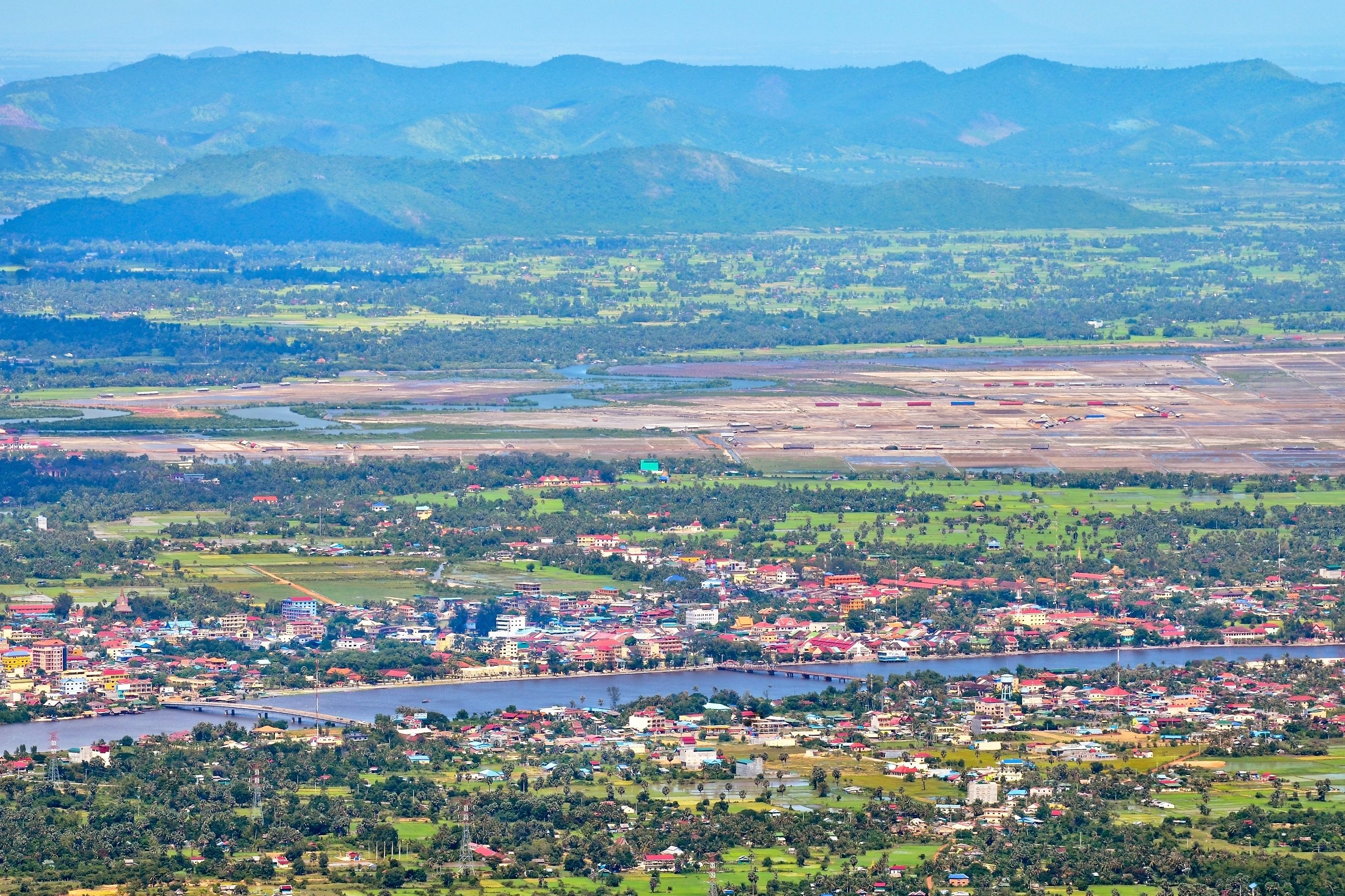 Uma vila costeira com um rio, edifícios e montanhas ao fundo.