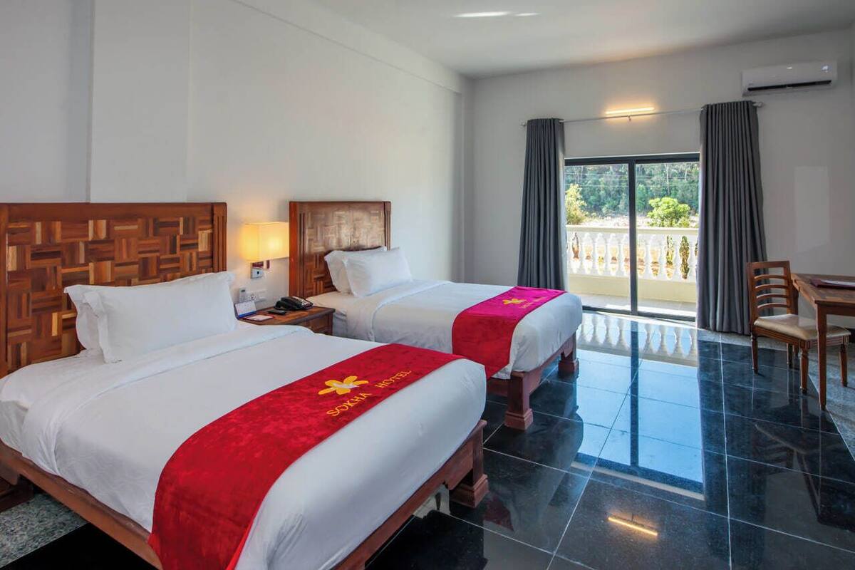 A hotel room with two beds, a balcony, and a dining area.