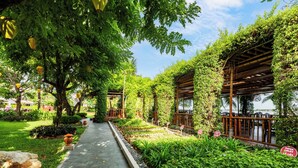 A pathway flanked by lush greenery and wooden pergolas, leading to a covered seating area. - Bel Marina Hoi An Resort (Da Nang)