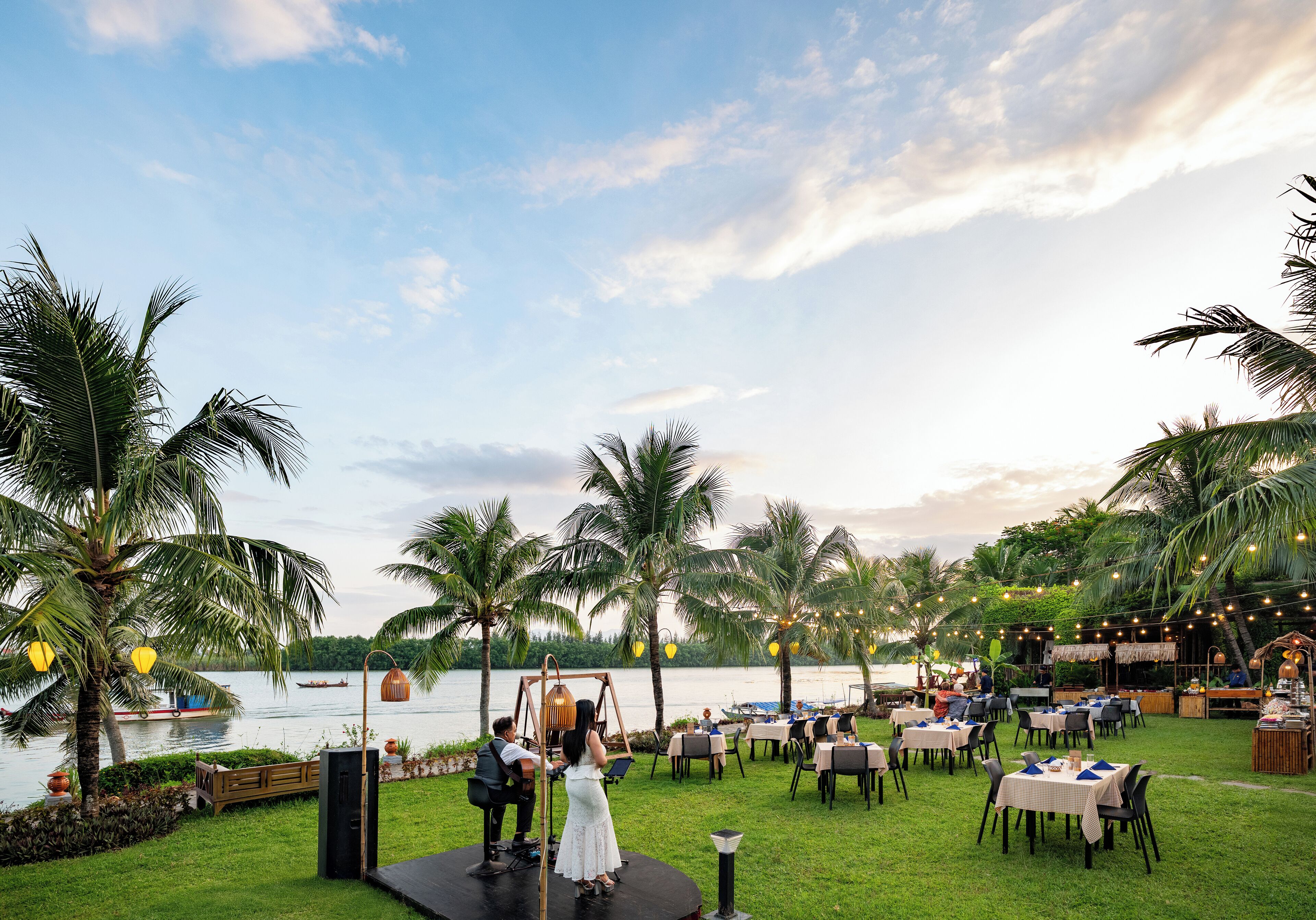 Un salón de bodas al aire libre con escenario, mesas y sillas, con vistas a un cuerpo de agua.