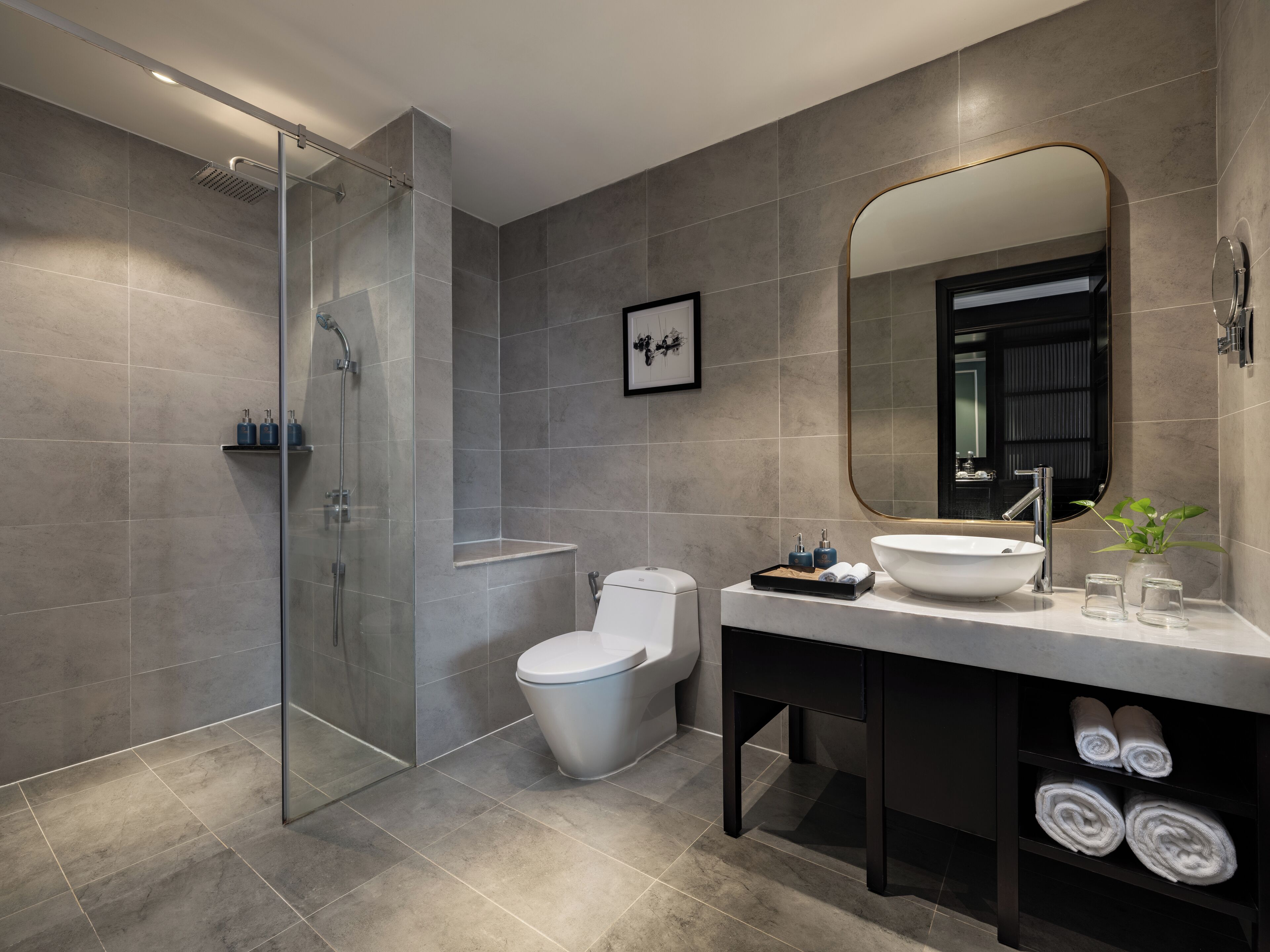 A modern bathroom with a glass-enclosed shower, a toilet, a sink with a large mirror, and neatly rolled towels in a shelf.