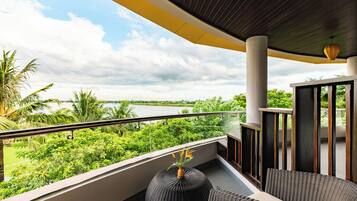 A balcony with a view of a river, surrounded by greenery, and furnished with wicker furniture.
