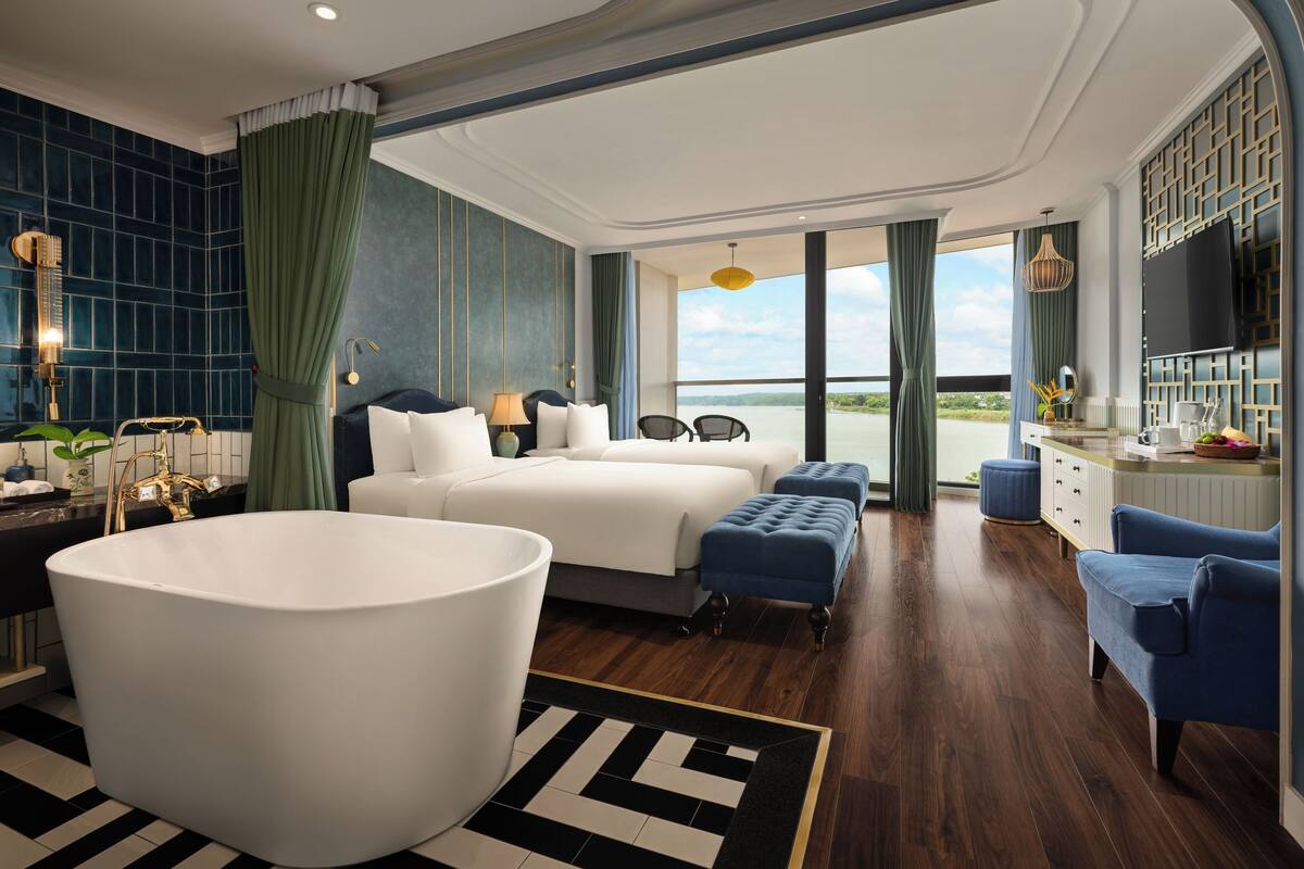 A spacious hotel room with a large bed, a bathtub, and a view of a body of water.