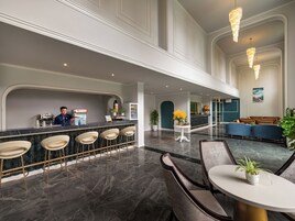 Un vestíbulo de hotel con mostrador de recepción, zona de bar, asientos y una escalera.