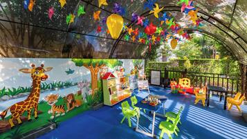 Zona de juegos infantiles con decoraciones coloridas, un mural y suelo azul.