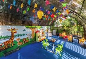 Zona de juegos infantiles con decoraciones coloridas, un mural y suelo azul.