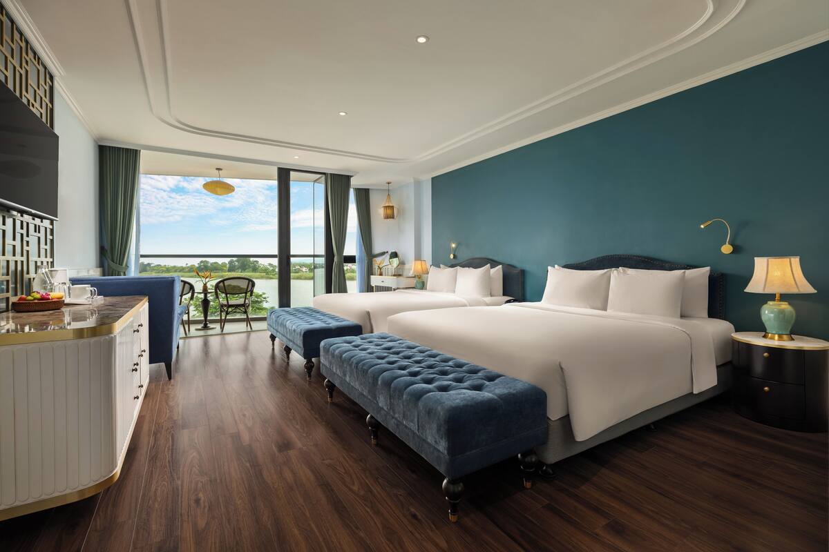 A hotel room with a large bed, a sitting area with a view, and a dining area with a view.