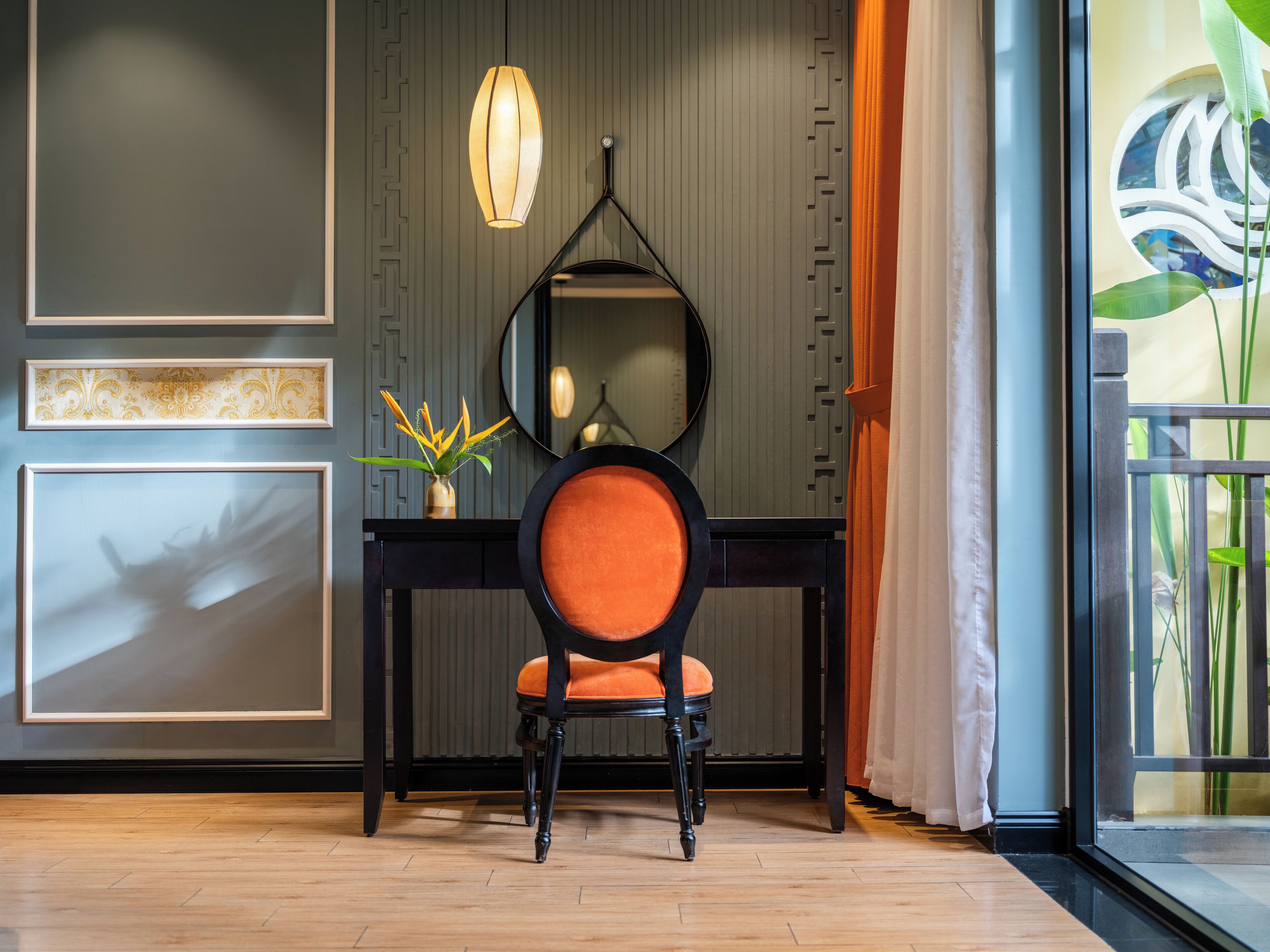 A modern interior with a wooden floor, a black desk with a round mirror, a vase with yellow flowers, and a hanging light fixture.