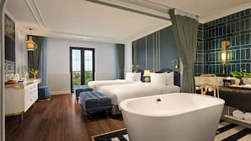 A modern hotel room with a large bathtub, two beds, a vanity with a mirror, and a view of the outdoors through a large window.