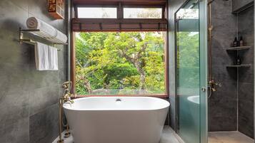 A modern bathroom with a freestanding bathtub, a glass shower enclosure, and a view of trees through a large window.