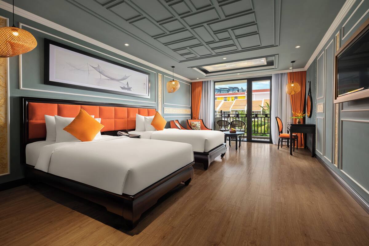 A hotel room with two beds, a dining area, and a balcony with a view.